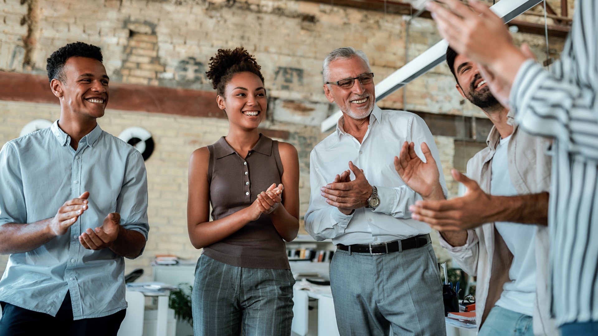 Congratulations! Multicultural team clapping their hands and smiling while standing in the creative office